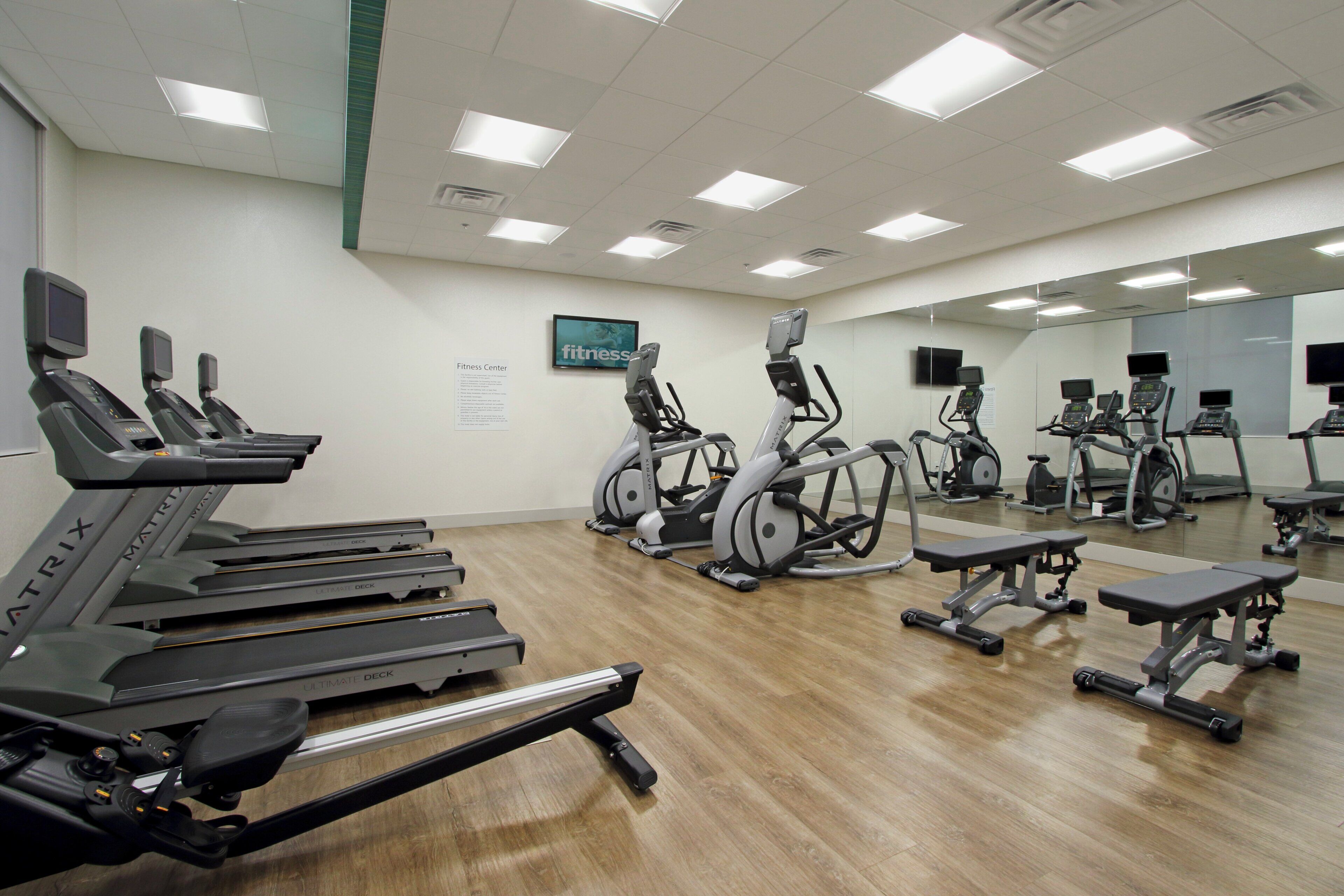 A fitness center with treadmills, elliptical machines, and a mirrored wall.