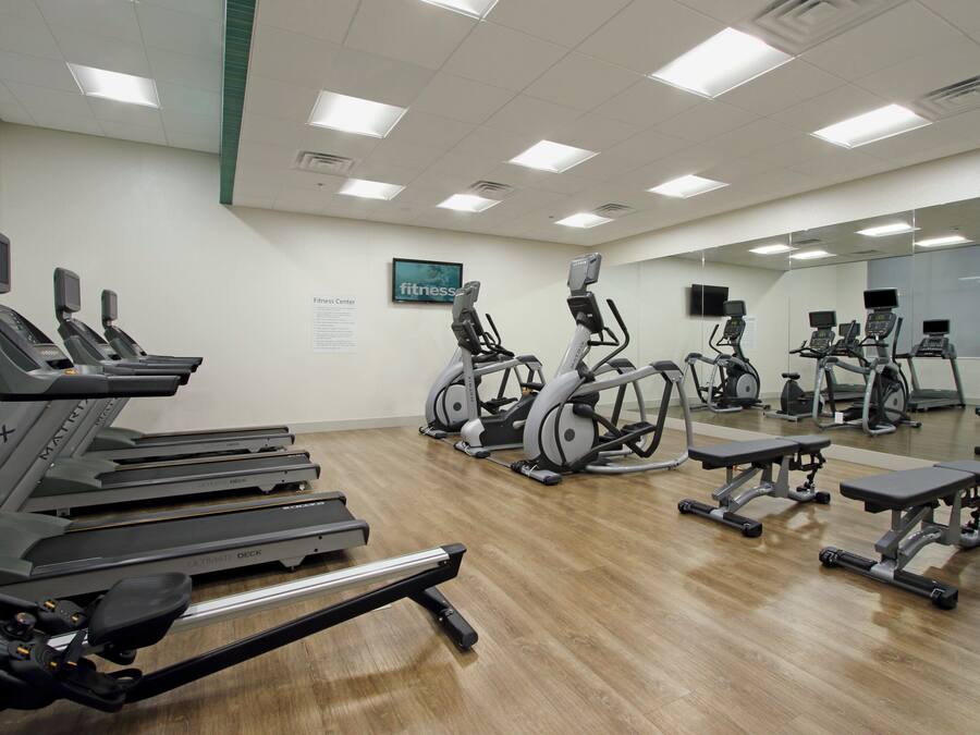 Un gimnasio con cintas de correr, elípticas y un espejo grande.