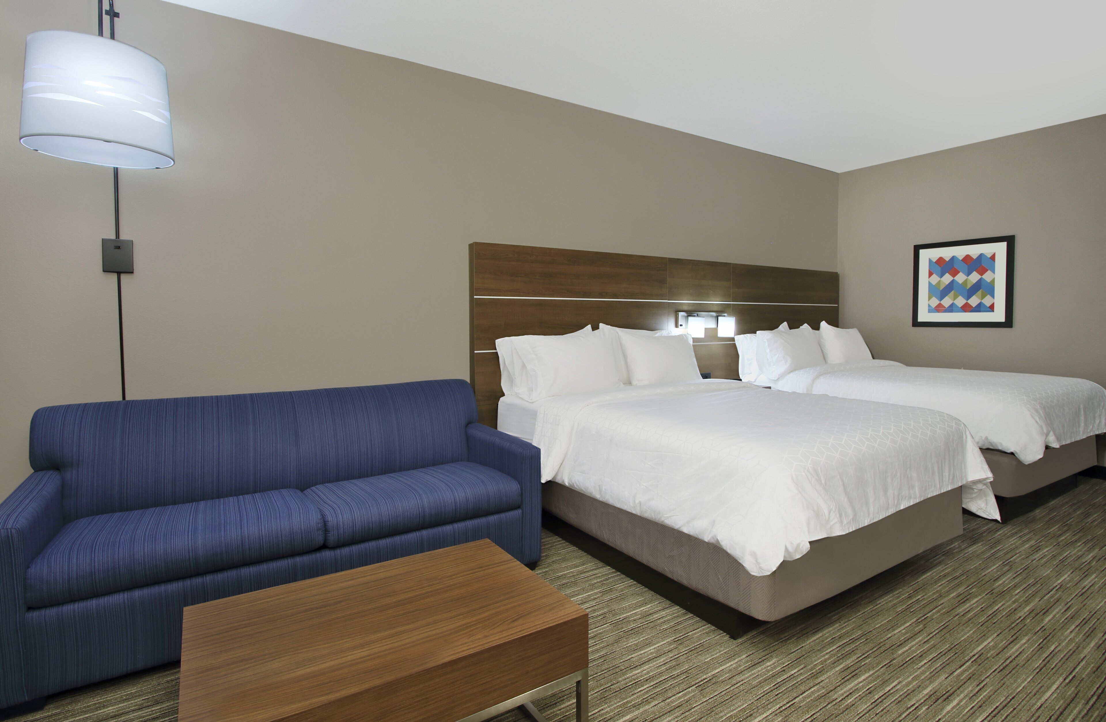 Ein Hotelzimmer mit zwei Betten, einem blauen Sofa, einem Holztisch und einer modernen Lampe.