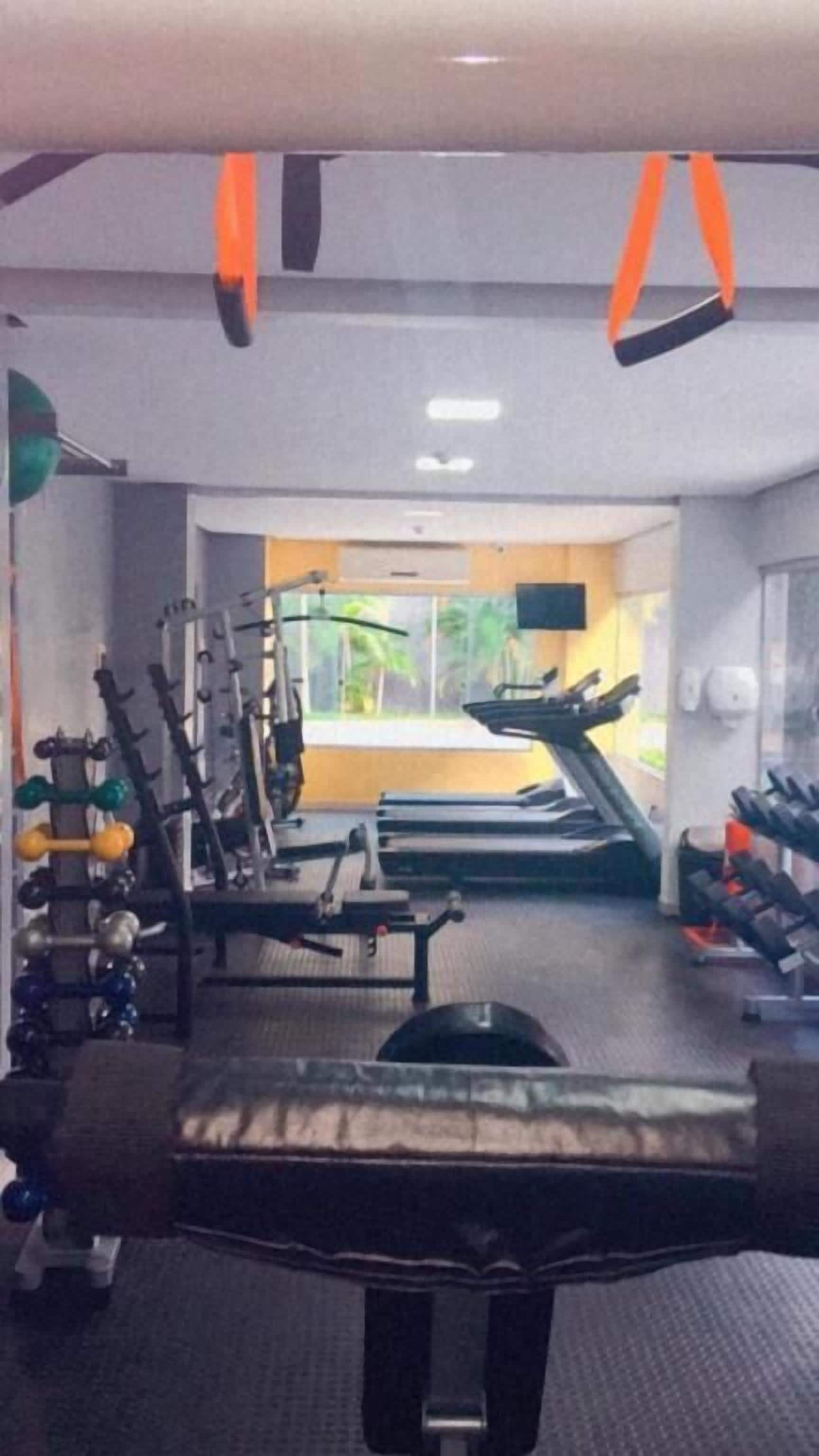 Un gimnasio con diverso equipo de ejercicio, incluyendo mancuernas, cinta de correr y máquinas de pesas.