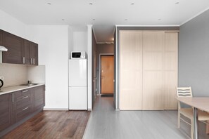 A modern kitchen with dark wood cabinets, a white refrigerator, and a wooden door leading to another room. - Tricolor Apartments (Moscow)