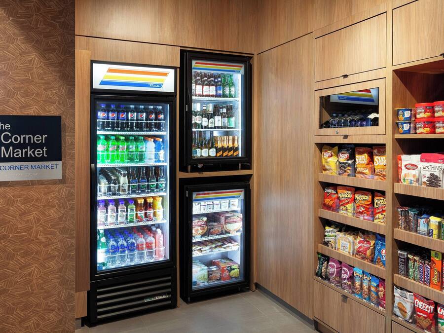 A corner market with refrigerated beverage dispensers and shelves stocked with snacks and cereals.
