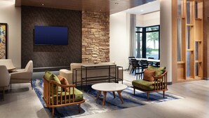 Un área de estar moderna con una pared de acento de piedra, un televisor de pantalla plana y un conjunto de asientos que incluye una mesa redonda y sillas acolchadas.