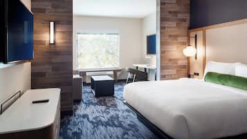 Ett hotellrum med en stor säng, ett skrivbord, en stol, en TV och ett fönster med utsikt över träd.