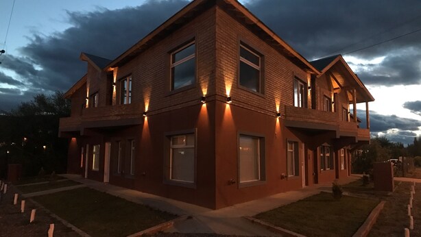 Uma casa de dois andares com fachada de tijolos e várias janelas, cercada por um gramado bem cuidado e uma entrada de automóveis com cascalho.