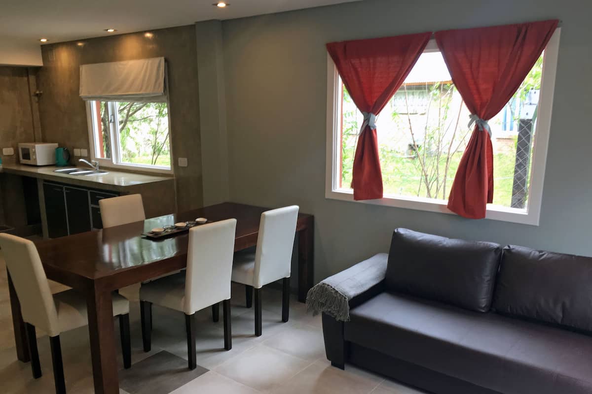 A modern living room with a dark brown sofa, a dining table with chairs, and a kitchen area with a microwave.