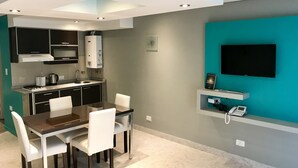 Cozinha moderna com forno embutido, micro-ondas e pia. Há uma mesa de jantar com cadeiras e uma TV de tela plana fixada na parede.