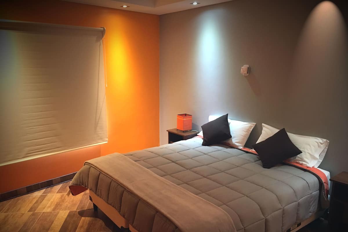 A bedroom with a bed, a nightstand, a lamp, and a window with blinds.