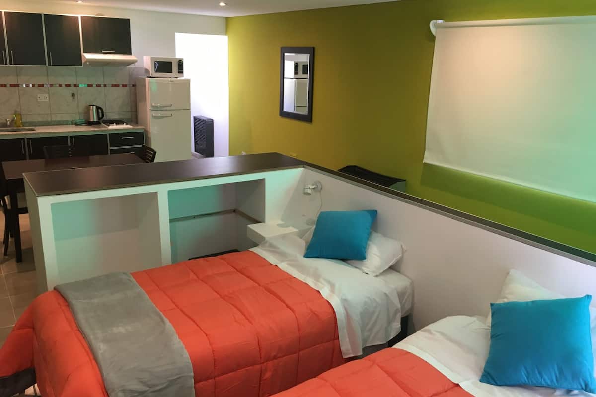 A compact hotel room with two beds, a kitchenette, and a small bathroom.