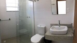 A bathroom with a glass-enclosed shower, a toilet, and a sink with a mirror above it. - Hotel Pousada Santos (Palhoça)