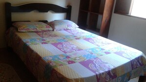 A bed with a floral quilt, a wooden headboard, and a window with curtains. - Sítio D. Tereza (Paraty)
