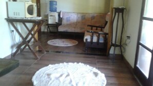 A small room with a wooden floor, a round rug, a sofa, a chair, a table with a microwave, and a water dispenser. - Sítio D. Tereza (Paraty)