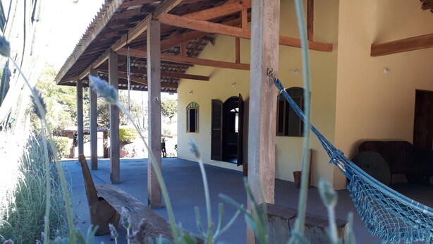 A covered outdoor area with wooden beams, a hammock, and a building with arched windows. - Sítio D. Tereza (Paraty)