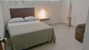 A bedroom with a bed, bedside table, lamp, and a chair. - Osean Oasis Luxury Apartment (Chicxulub Pueblo)