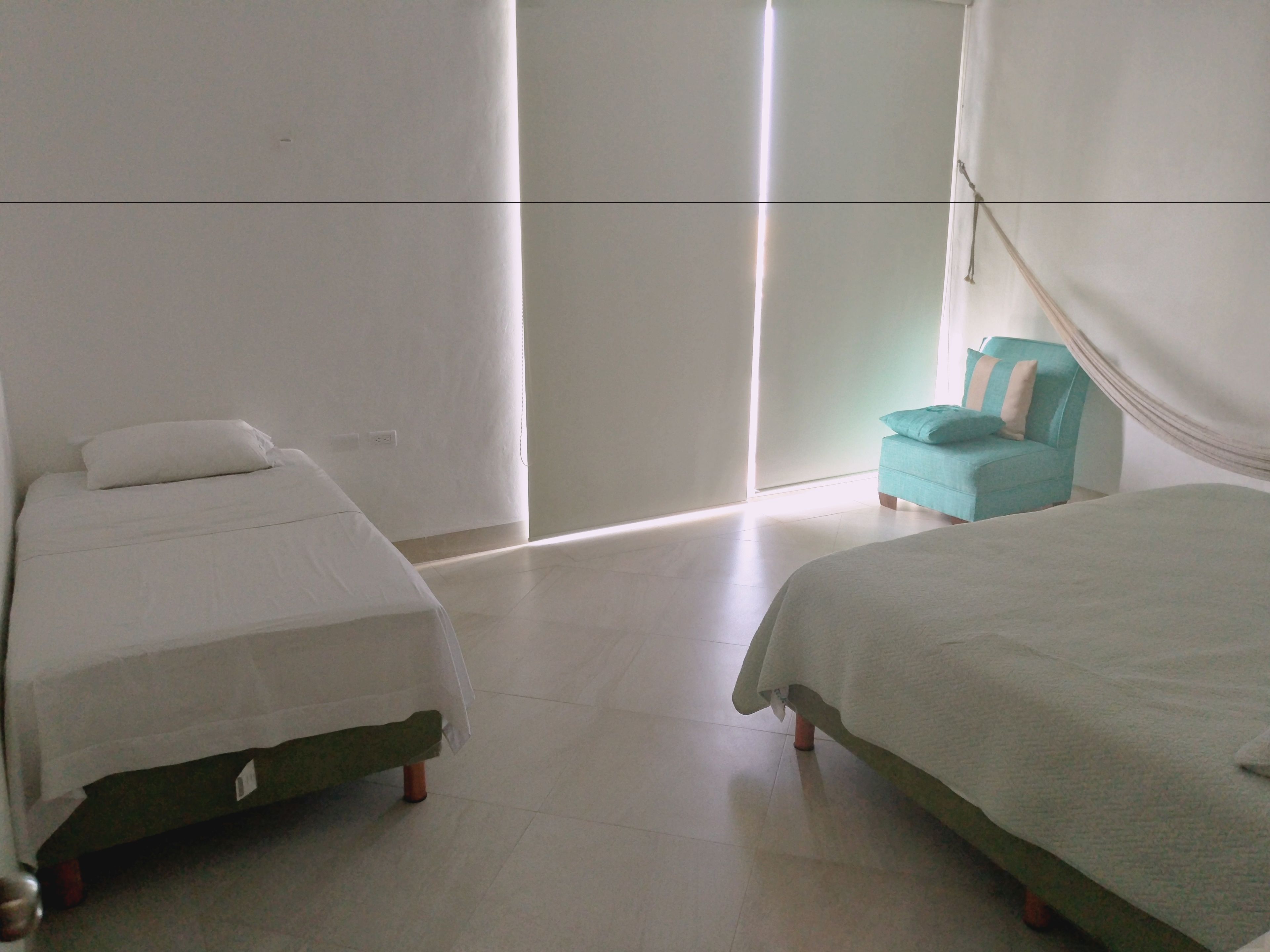 Ein Zimmer mit zwei Betten, einem Sessel und einem großen Fenster.