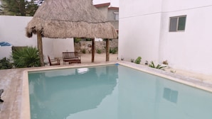 A rectangular swimming pool with a thatched roof structure nearby. - Osean Oasis Luxury Apartment (Chicxulub Pueblo)