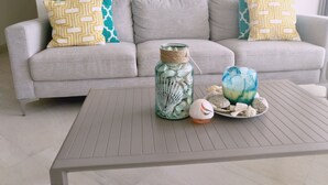 A modern living room with a grey sofa, patterned cushions, a glass jar with stones, and decorative vases on a wooden coffee table. - Osean Oasis Luxury Apartment (Chicxulub Pueblo)