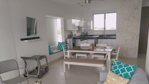 A modern living room with a grey sofa, a coffee table, and a dining area with a table and chairs. - Osean Oasis Luxury Apartment (Chicxulub Pueblo)