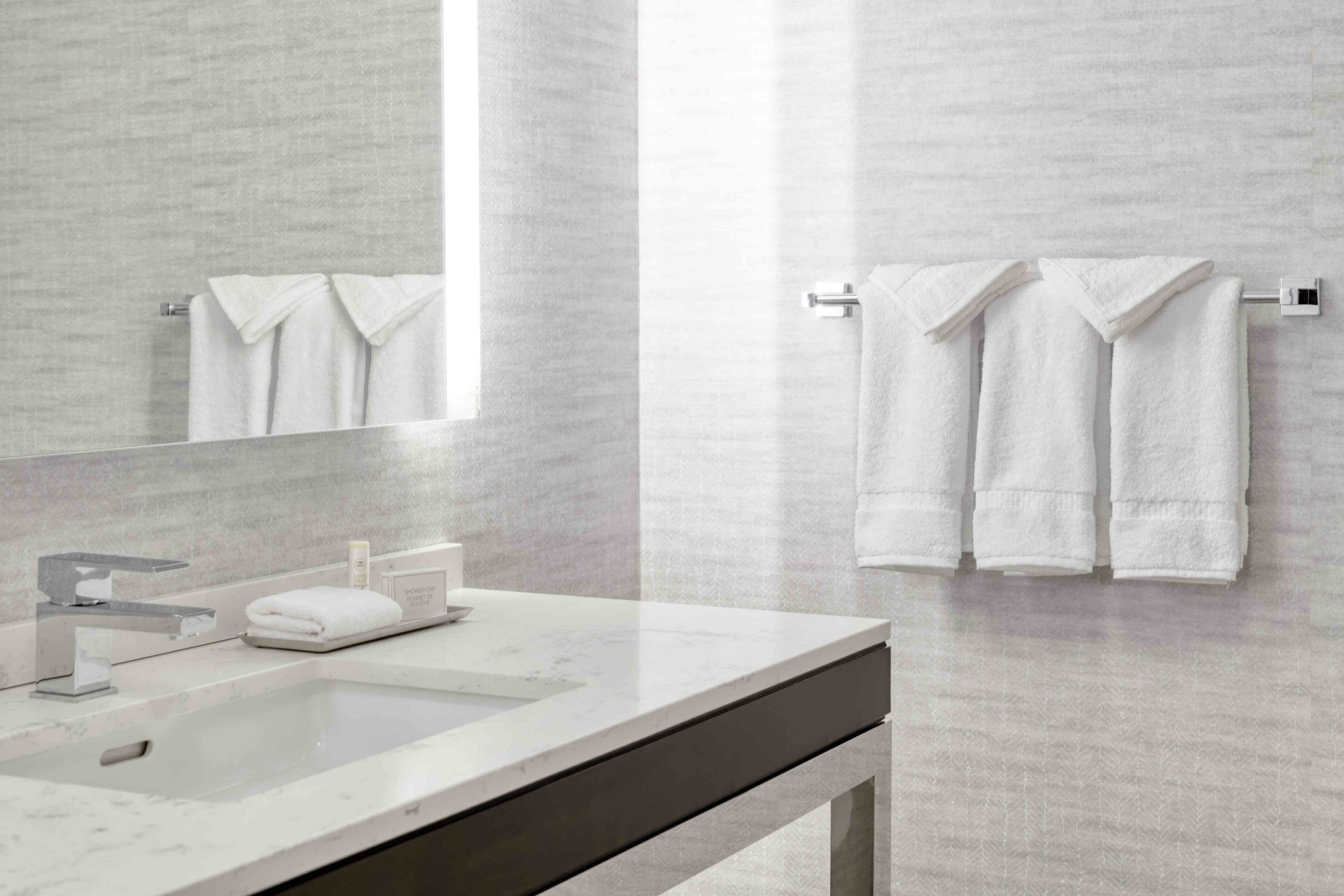 A modern bathroom with a marble sink, a large mirror, and two towels hanging on a towel rack.