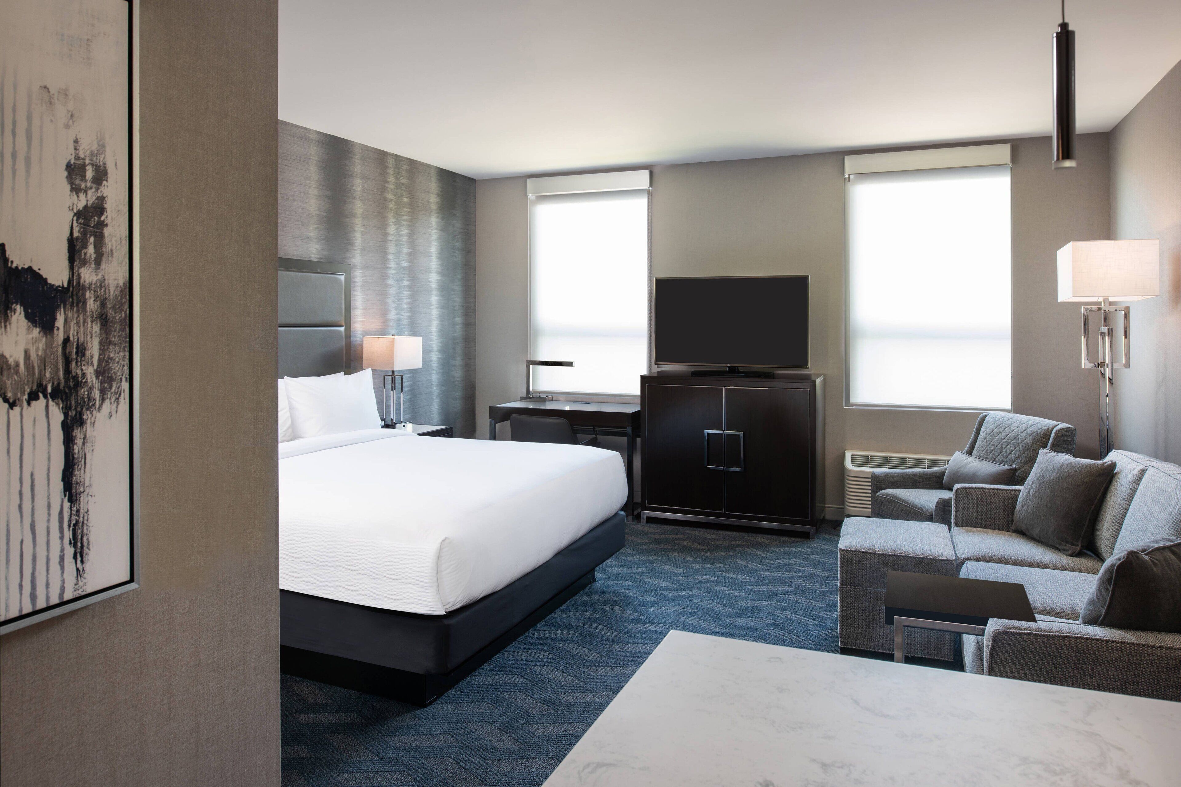 A hotel room with a large bed, a desk, a TV, a sofa, and a painting on the wall.