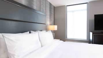 Quarto de hotel com uma cama grande, televisão de tela plana, janela com cortinas e abajur em uma mesa de cabeceira.