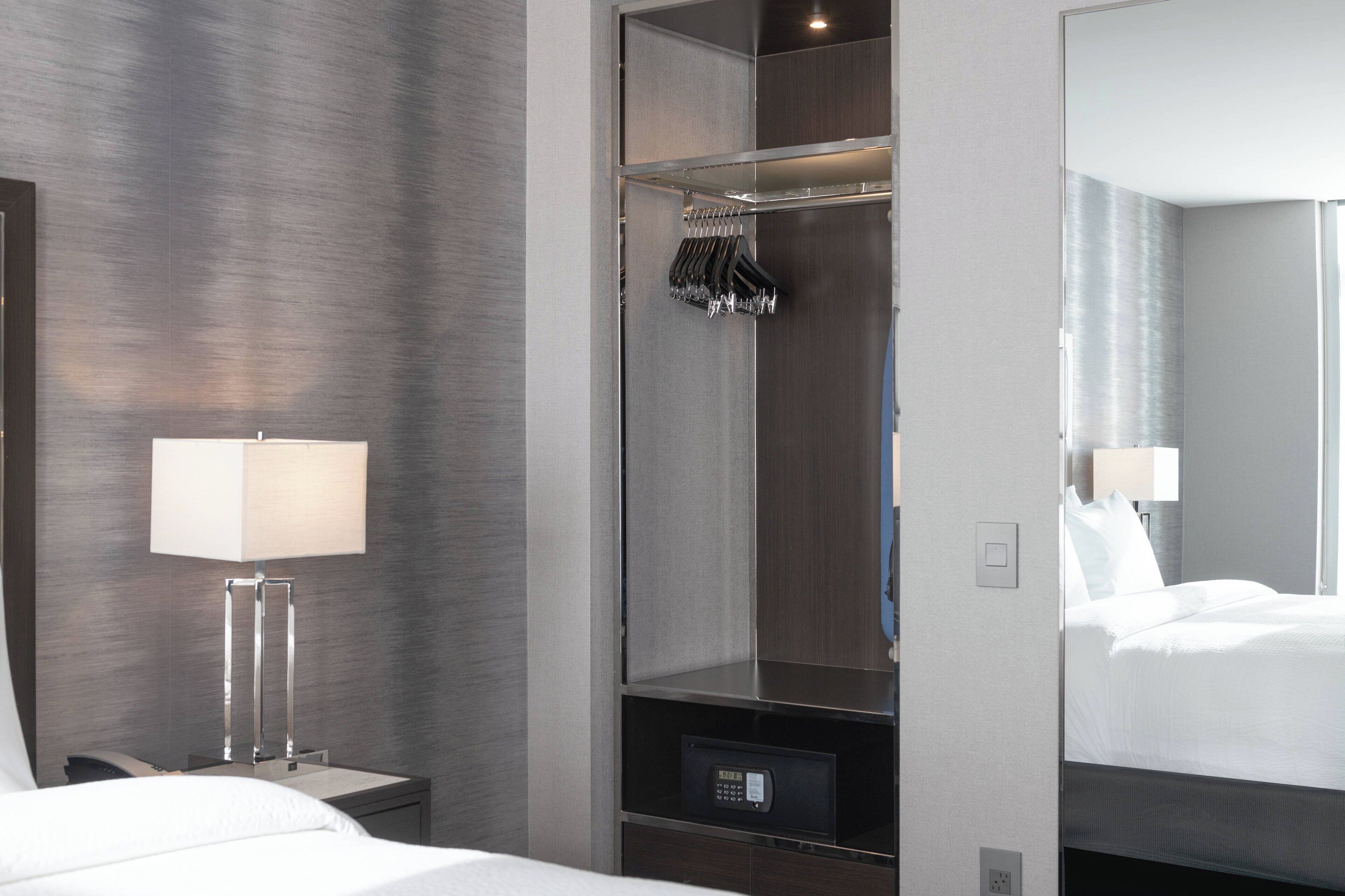 Camera d'albergo con un letto, un comodino con una lampada, un armadio pieno di abiti e uno specchio che riflette il letto.