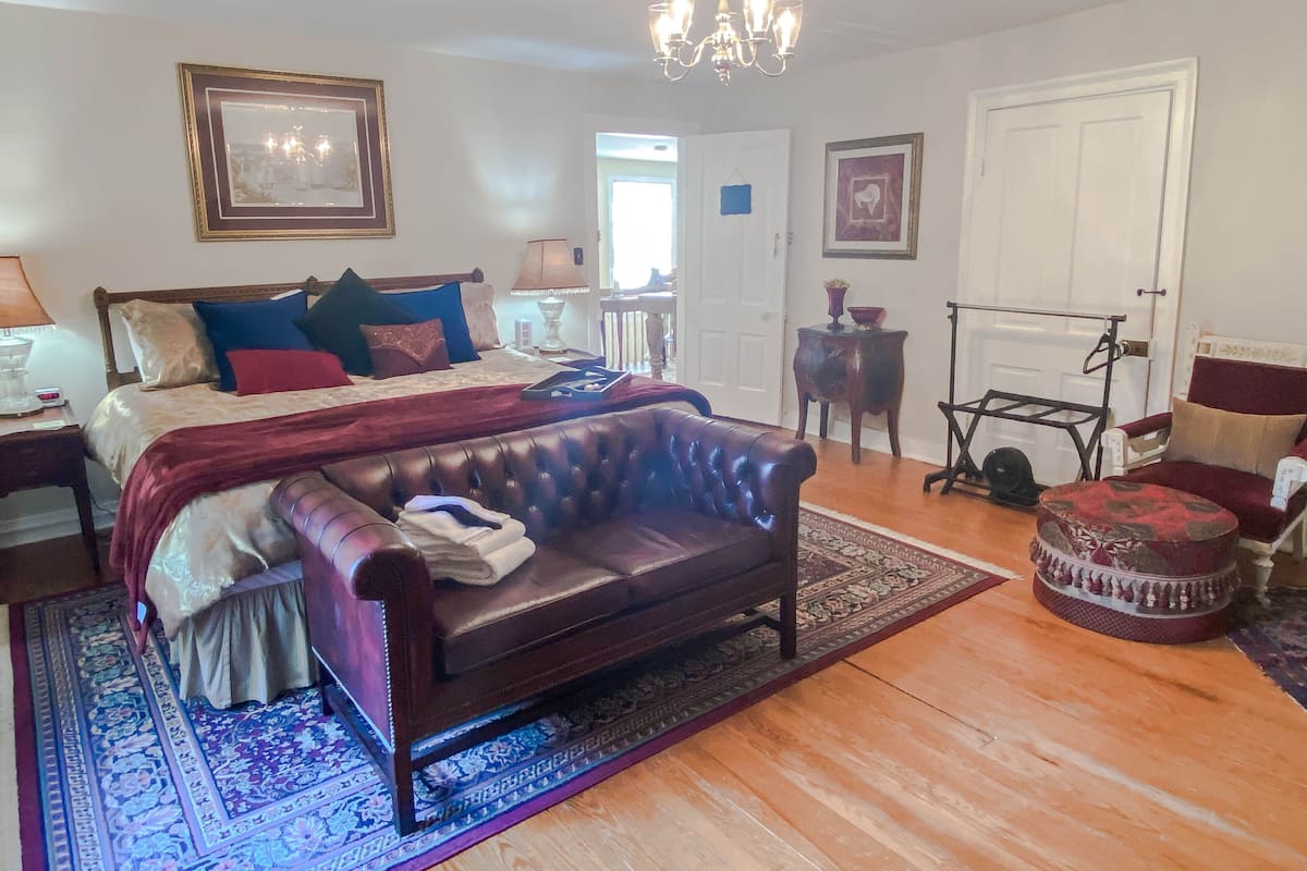A bedroom with a large bed, a leather sofa, a chandelier, and a wooden floor.