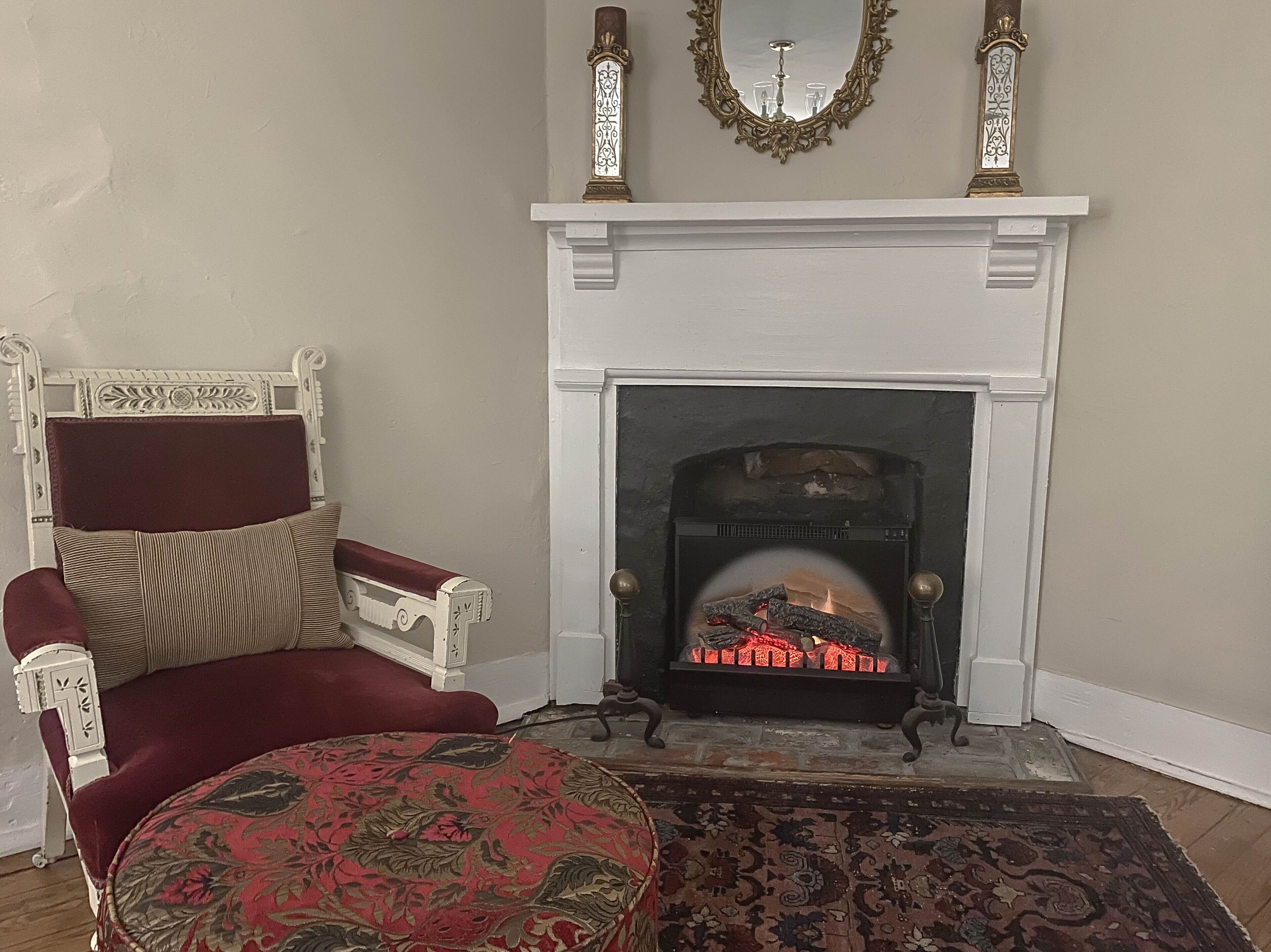 A room with a white fireplace, a red armchair, and a patterned rug.