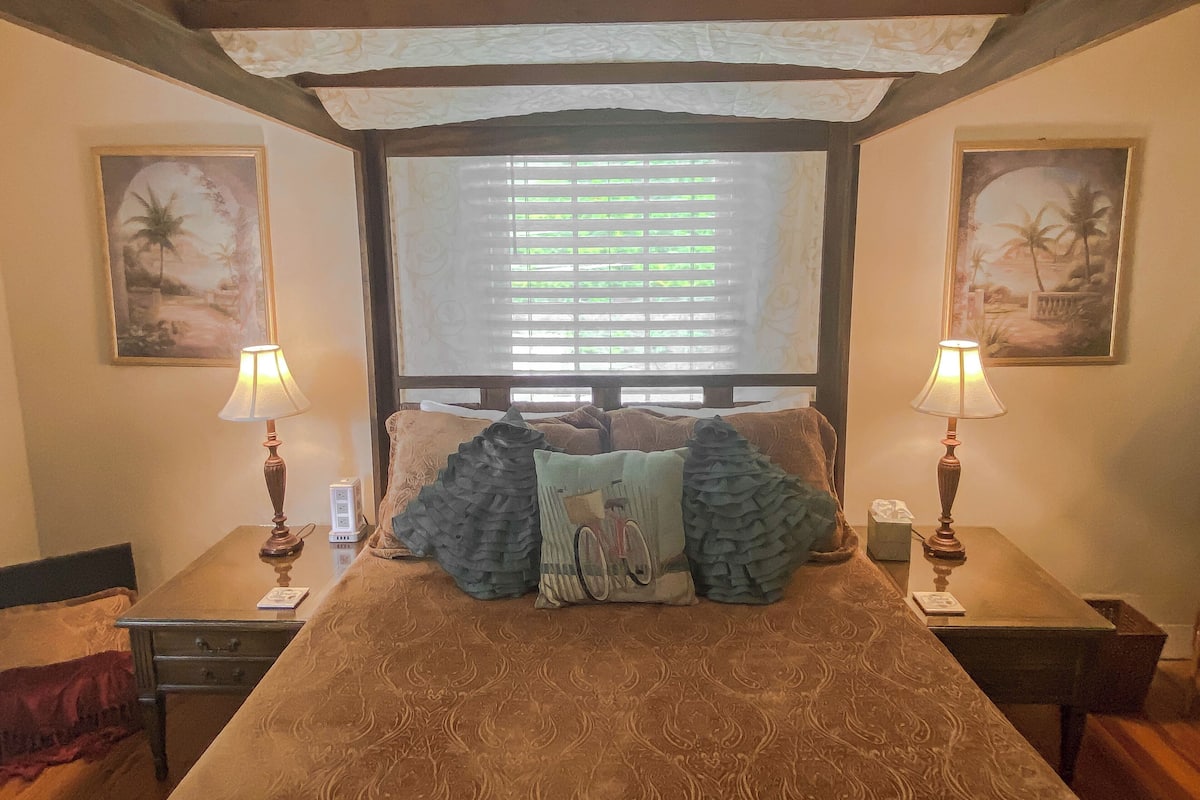 A bedroom with a large bed, two bedside tables, two lamps, and two framed pictures on the walls.