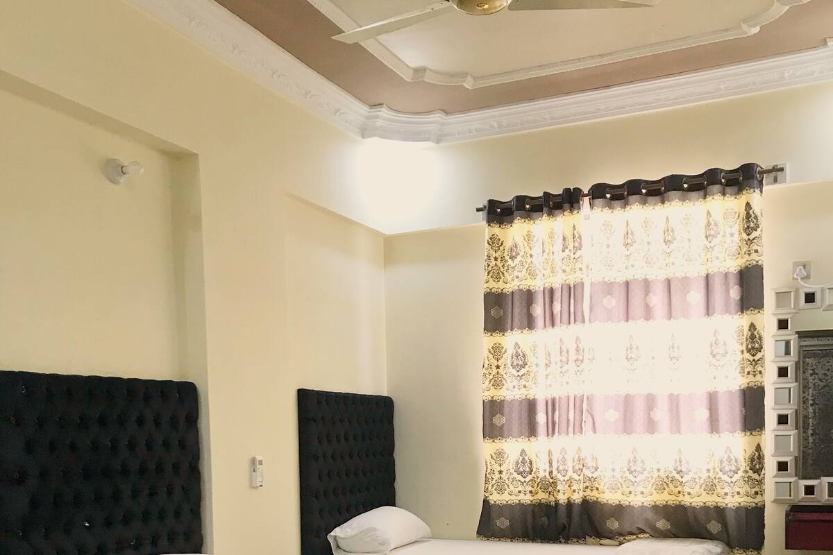 A hotel room with two beds, a ceiling fan, a TV, and a large window with curtains.