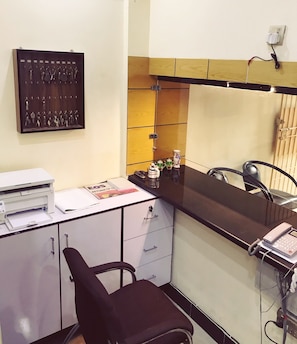 A reception desk with a printer, a chair, a key rack, and a small shelf with decorative items. - Hotel Second Home (Karachi)