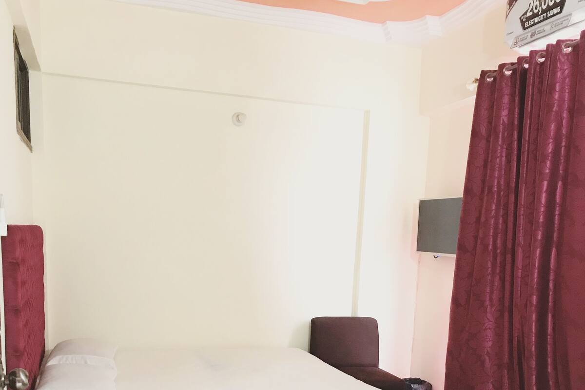 A hotel room with two beds, a nightstand, a lamp, and a wall-mounted TV.