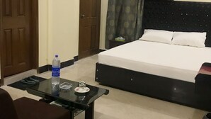 Una habitación de hotel con cama, una mesita con una botella y un vaso, una silla y dos puertas.