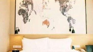 A hotel room with a large bed, a headboard with a world map, and a nightstand with a lamp. - Kyriad Hotel (Guangzhou)