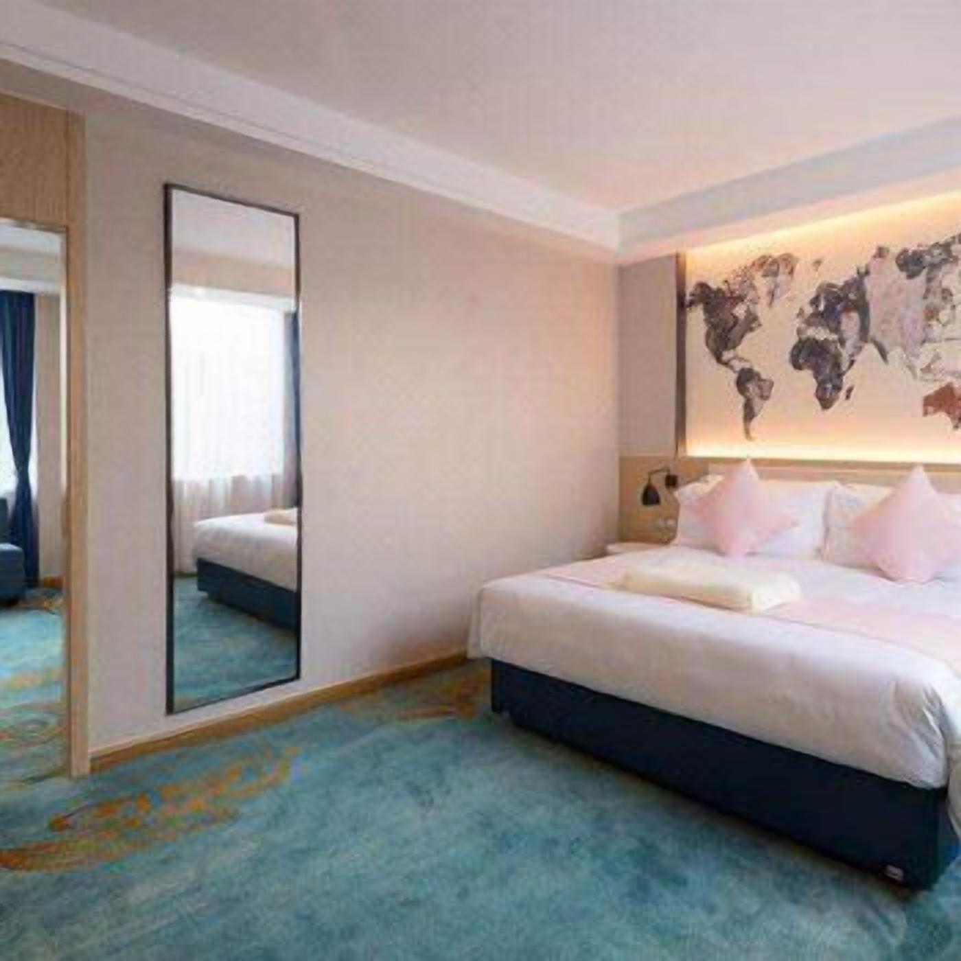 A hotel room with a large bed, a world map on the wall, a mirror, and a blue carpet.