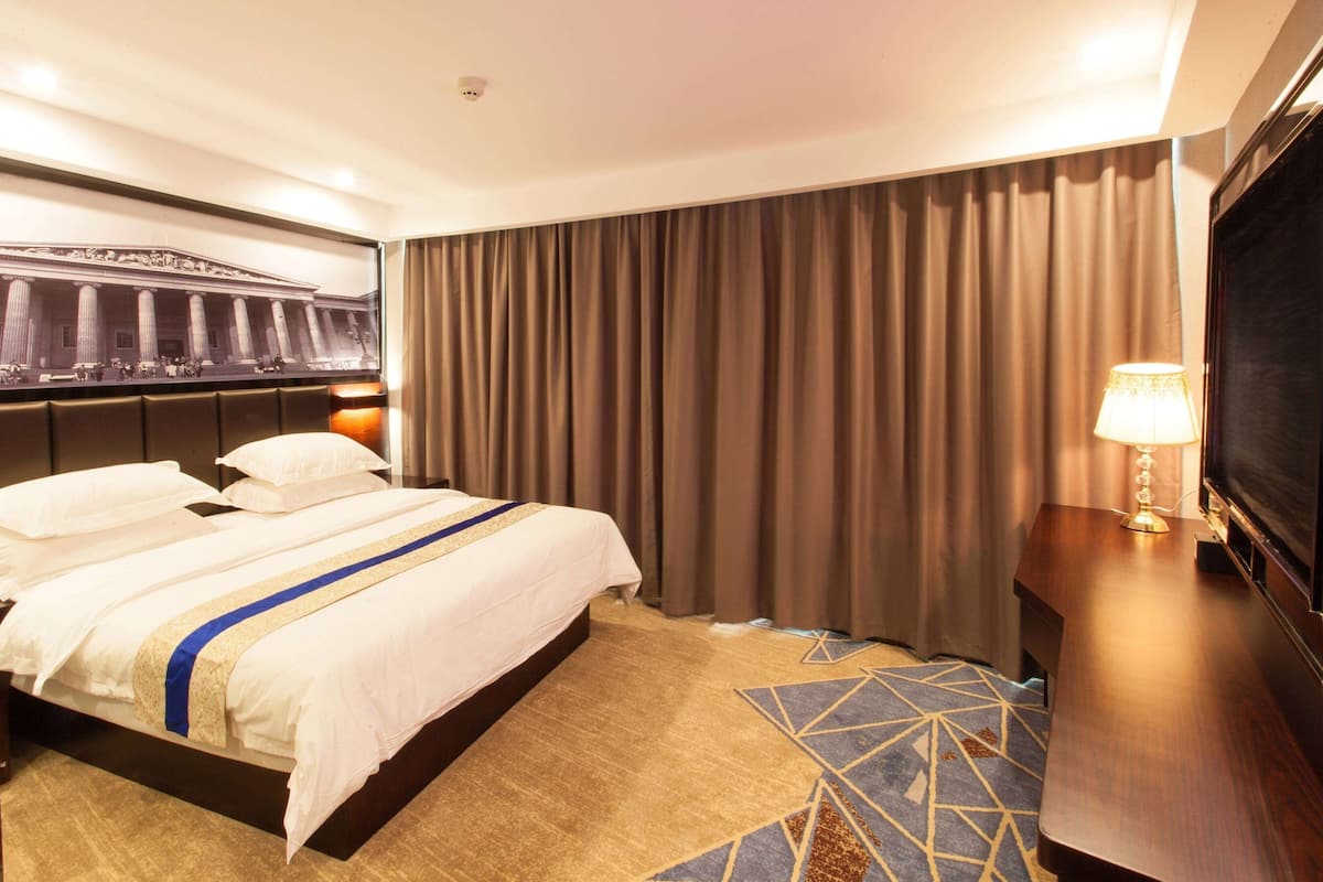 Een hotelkamer met een groot bed, een televisie, een lamp en een kunstwerk aan de muur.