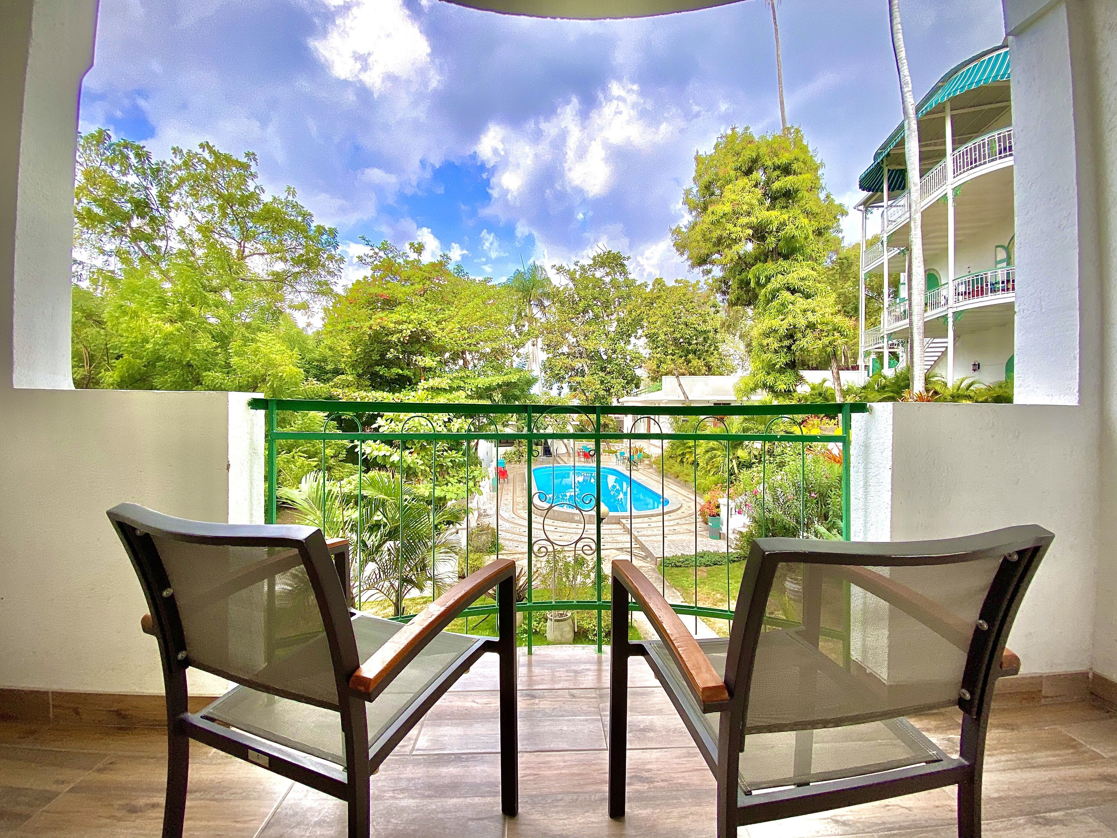 A balcony with two chairs, a pool, and a building with balconies in the background.