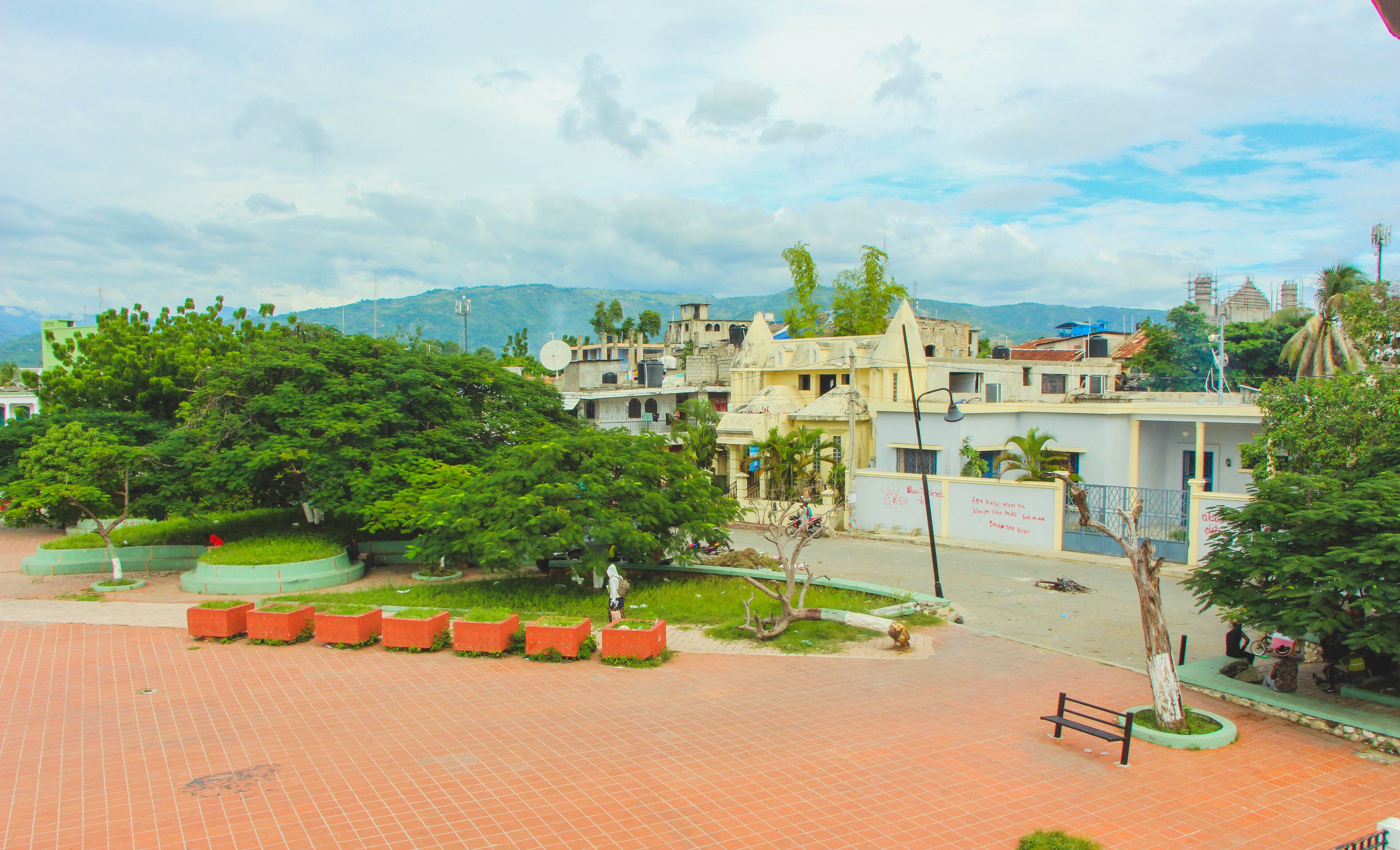 A paved public square with a bench, trees, and buildings in the background.