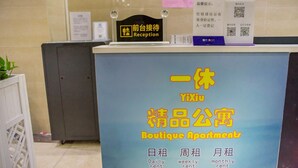 Un mostrador de recepción con un cartel que indica 'Reception' y un cartel para 'Yixiu Boutique Apartments' con opciones de alquiler diario, semanal y mensual.