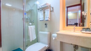 Un baño con ducha de vidrio, inodoro, lavamanos con espejo y perchero para toallas.