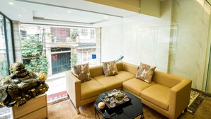 A modern living room with a beige sofa, decorative pillows, a glass coffee table, and a statue. - Golden hotel (Hanoi)