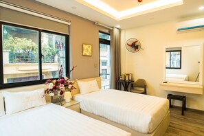 Habitación de hotel con dos camas, una mesita con una silla, una ventana con vistas al exterior y un ventilador fijado a la pared.