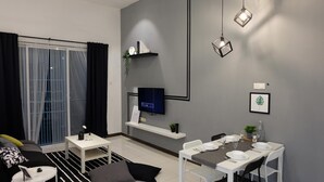 A modern living room with a sofa, a coffee table, a TV mounted on the wall, and a dining area with a table set for two. - Skypod (Puchong)