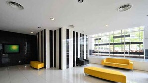 A modern lobby with a large window, a flat-screen TV, and yellow seating. - Skypod (Puchong)
