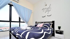 Une chambre avec une grande fenêtre, un lit recouvert d’une couette à rayures bleu marine et blanches, une table de chevet avec une plante, et un autocollant mural qui dit : « tout ce dont vous avez besoin, c’est de dormir ! »