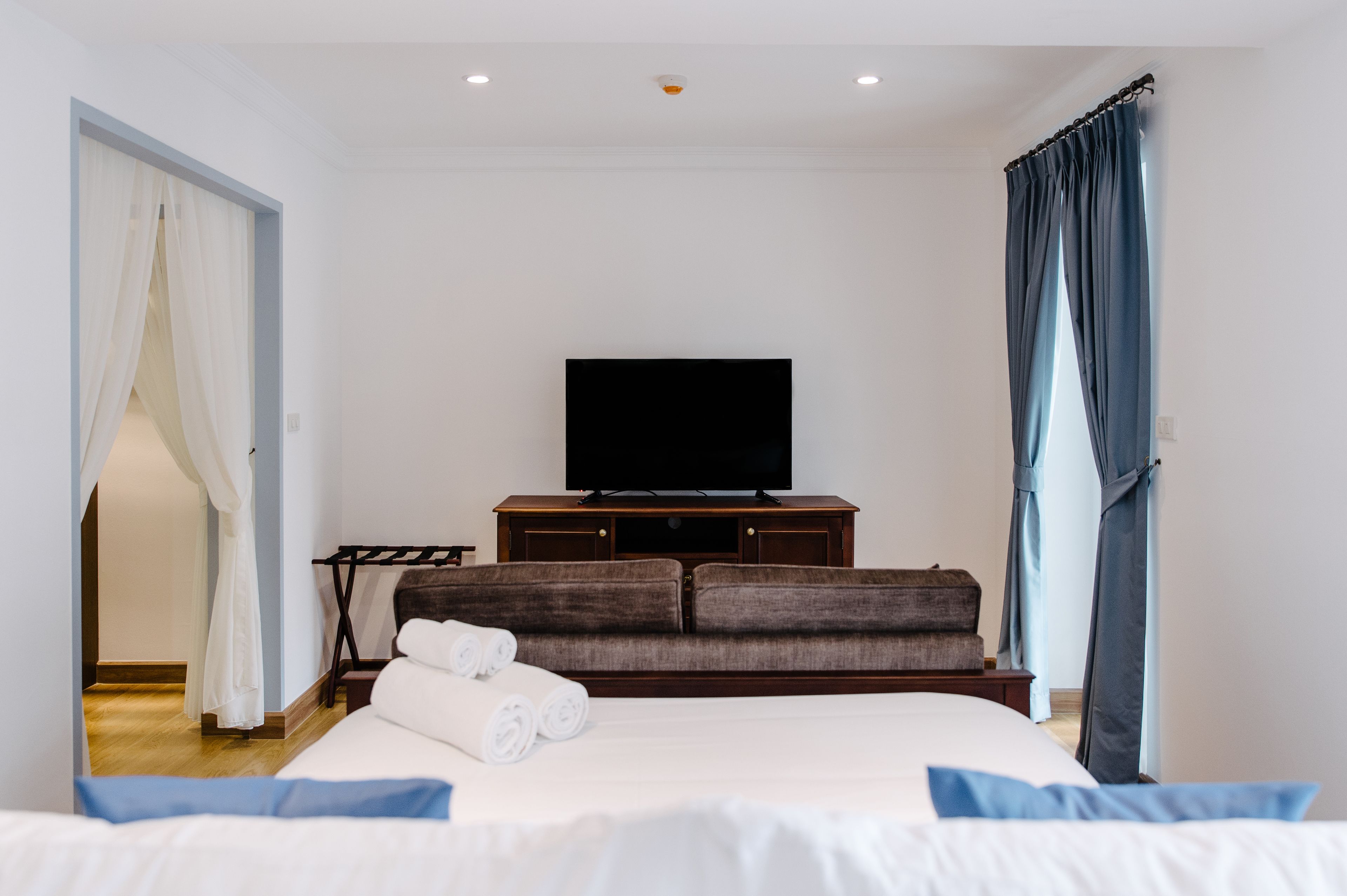 A hotel room with a bed, a TV on a wooden stand, a sofa, and a curtain.