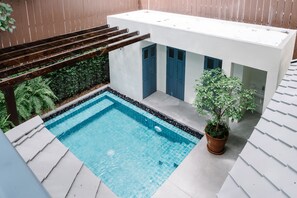 A modern outdoor pool area with a clear blue pool, a small building with blue doors, and a potted plant. - Baan Vajra (Bangkok)