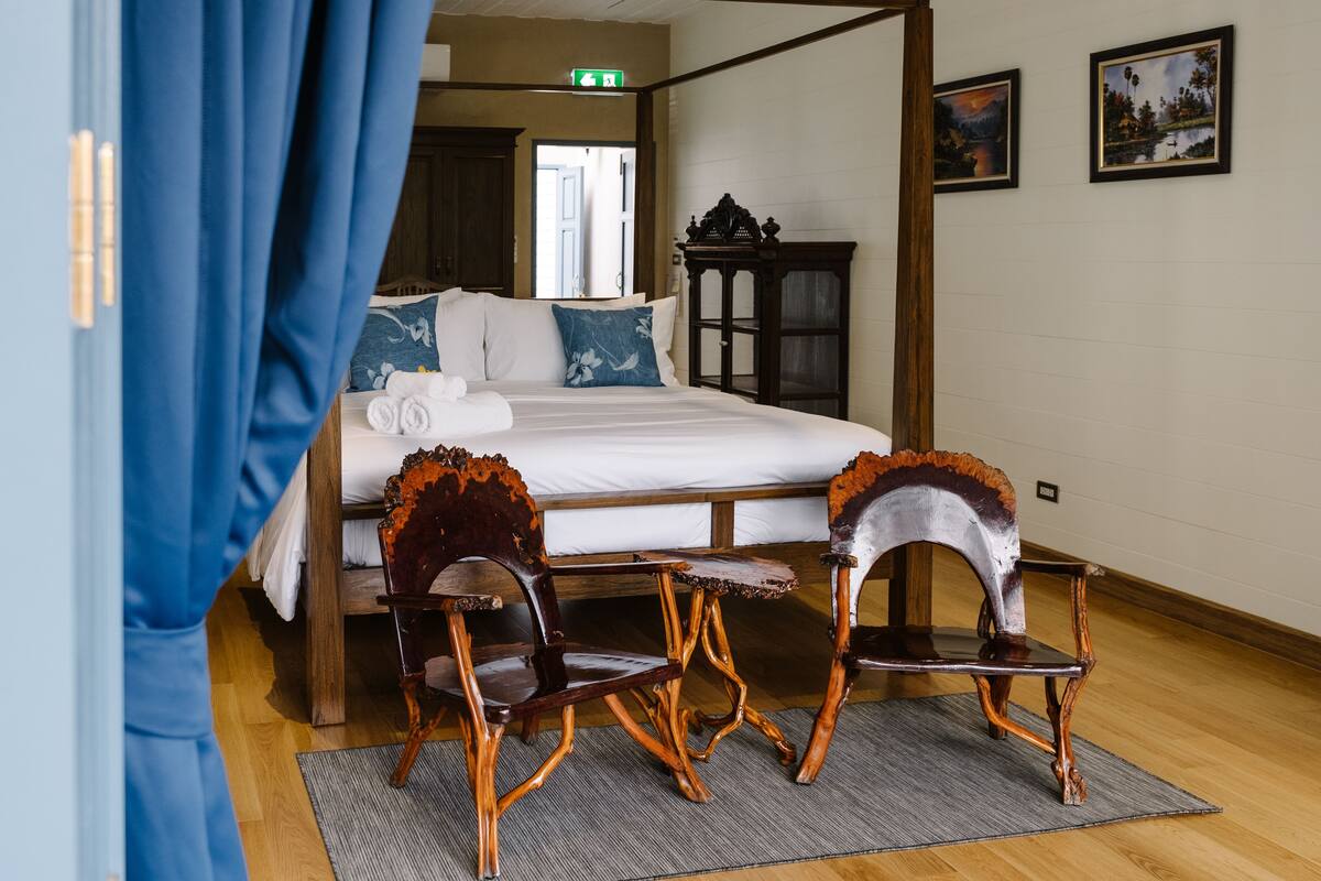 Ein Schlafzimmer mit einem Himmelbett, zwei Schaukelstühlen, einer Holzkabine und zwei gerahmten Bildern an der Wand.