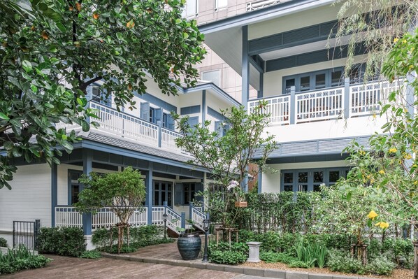 A multi-story building with balconies, a covered walkway, and a garden area with various plants and a large planter. - Baan Vajra (Bangkok)