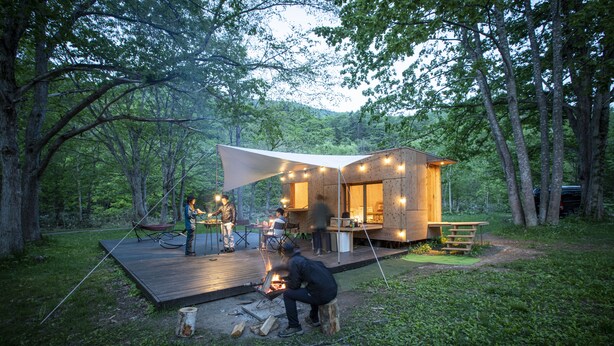 Una cabaña de madera con terraza, un hoyo de fuego y luces colgantes.